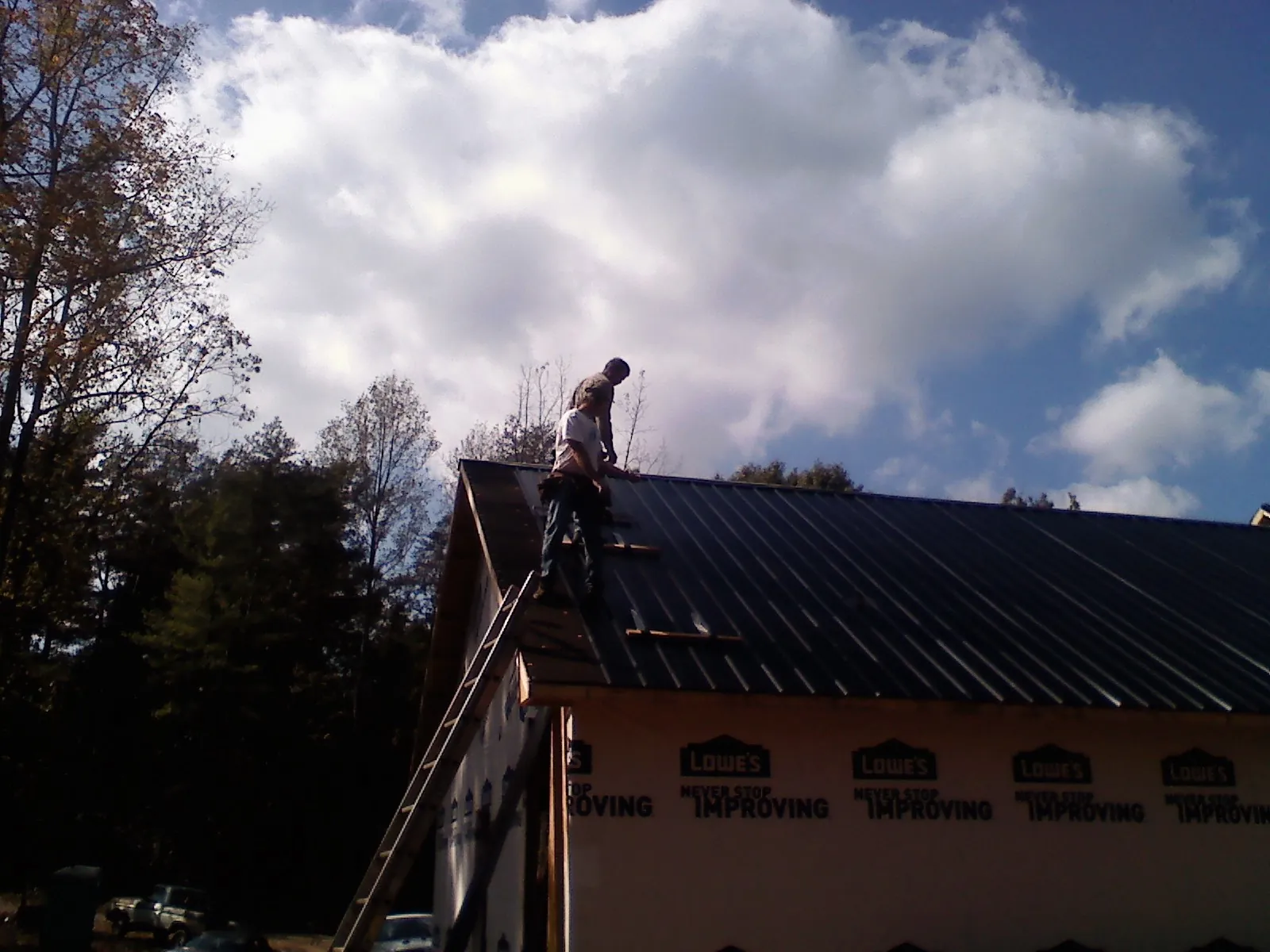 Roofer fastening dark metal panels high against a cloudy sky, from a Roof Inspection job in Scottsburg