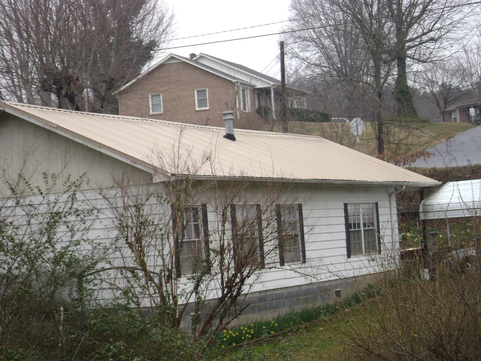 Tan metal roof on a white sided house set into a hillside — Commercial Roofing by Roofing Brothers in Scottsburg